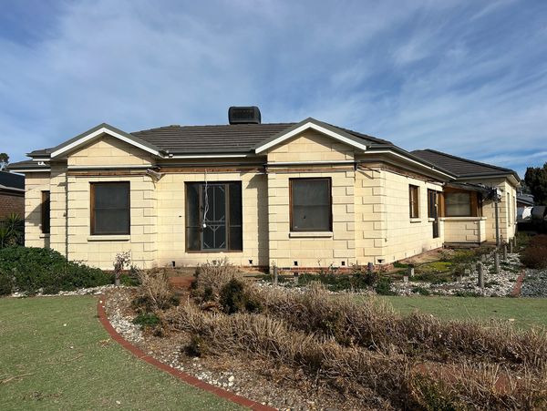 Single-story cream house with a tiled roof under a partly cloudy sky.