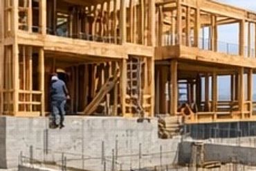 Wooden frame house under construction on a hillside with concrete foundation.