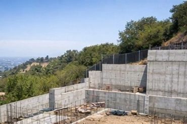 Concrete foundation construction on a hillside with city view.
