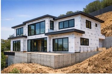 Modern house under construction with large windows and concrete foundation.