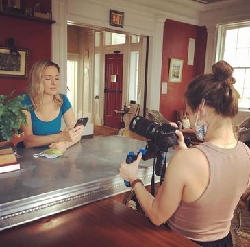 Woman filming another woman sitting at a table with phone.