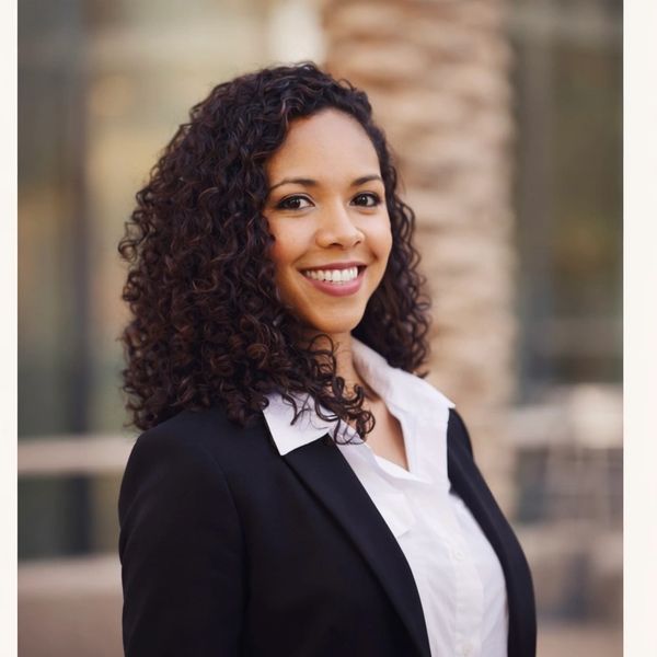 Confident professional woman with curly hair smiling outdoors.
