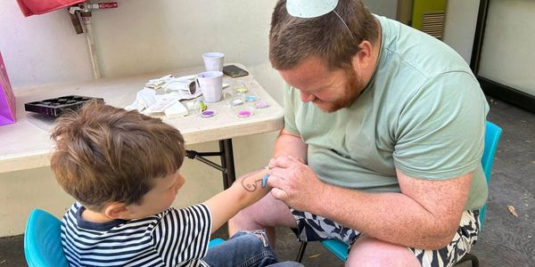Man painting a tattoo on a boy's arm.
