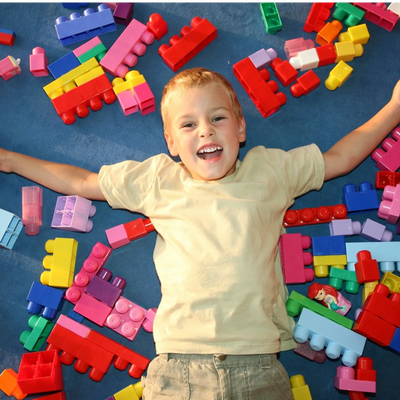 Happy young boy laying on floor among toy construction blocks