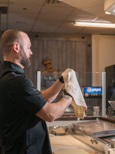 A mount shasta pizzeria employee making a pizza using handmade dough.