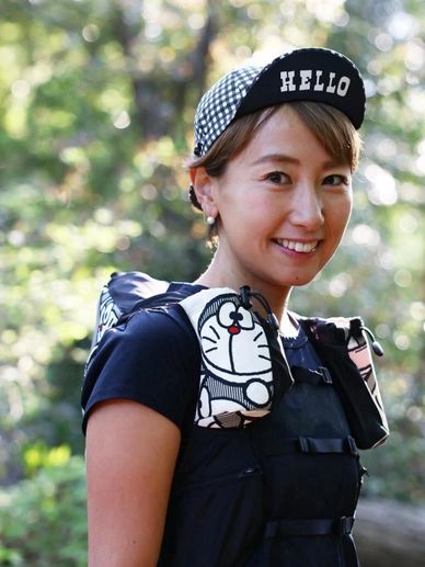 Smiling woman wearing a black cap with 'HELLO' and Doraemon-themed shoulder bags.