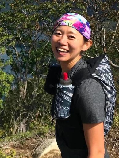 Smiling woman hiking outdoors with a colorful headband and hydration pack.