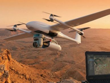 A drone flying over a rocky landscape at sunset with a laptop showing flight data.