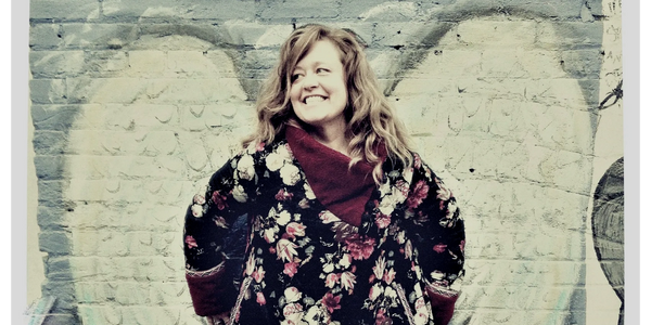 Woman Julie Fogerson in front of brick wall, angel wings.