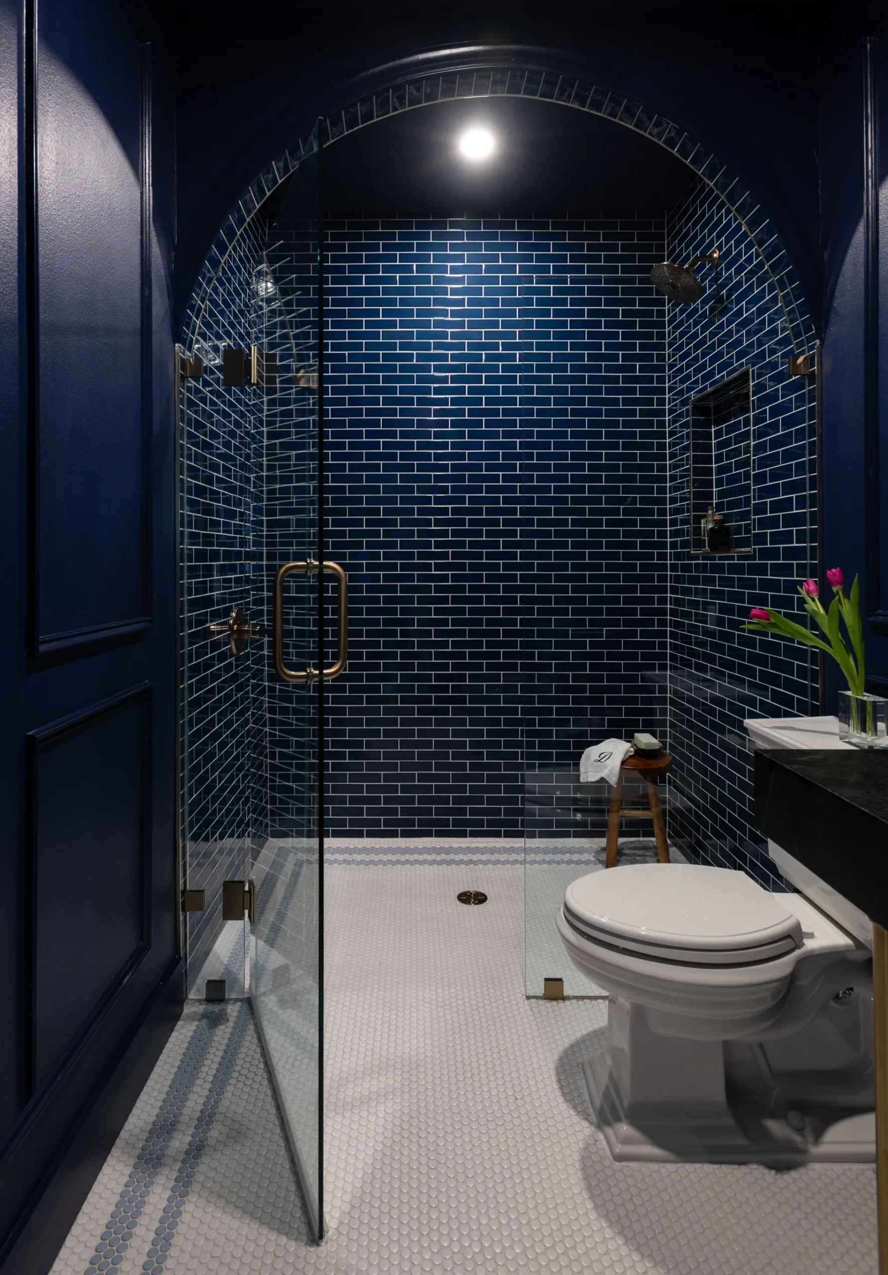 Custom arched navy subway tile shower with brass fixtures & penny tile floor by Gold Standard Contra