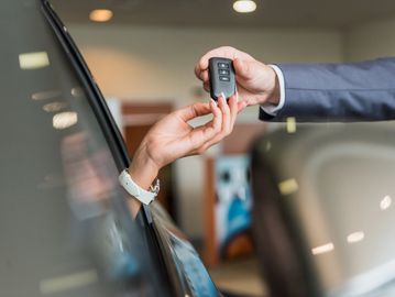 Person handing over car keys to another person inside a car.