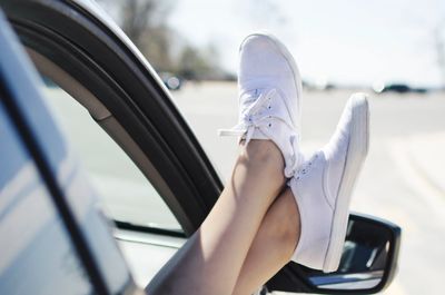 Person relaxing with feet out the car window wearing white sneakers.