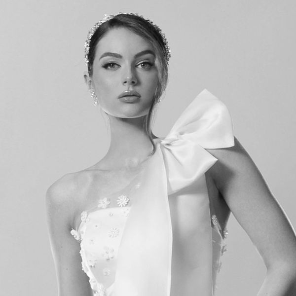 Bride wearing short wedding gown with bow and sheer floor-length overlay with floral embellishment.