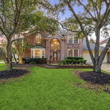 Elegant brick house with lush green lawn and mature trees at dusk.