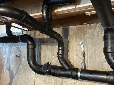 Black PVC plumbing pipes installed along a concrete wall in a basement.