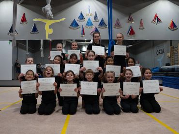 Young gymnasts proudly holding certificates in a training gym.