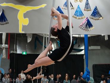 A girl performs aerial silks in front of an audience in a gym.