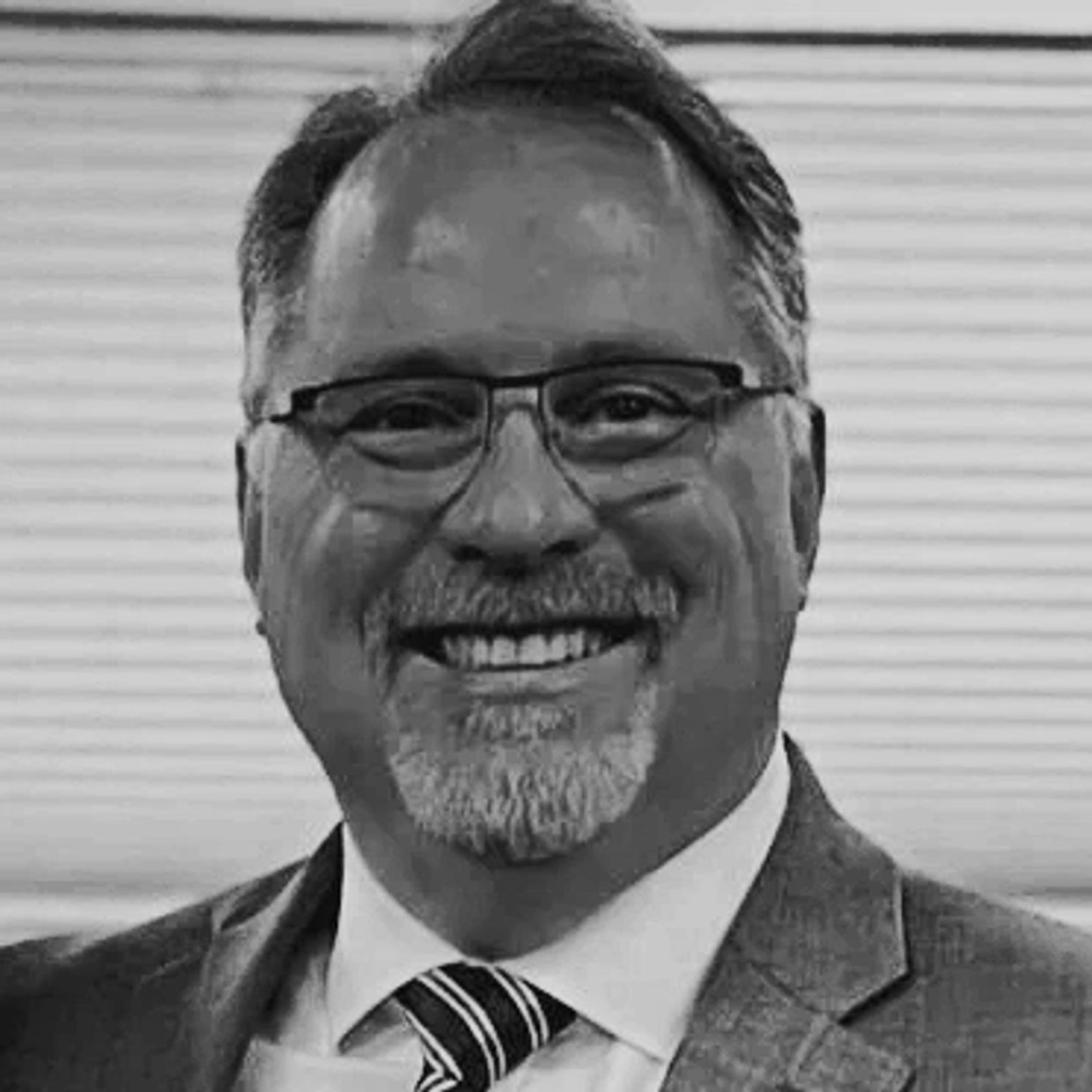 Smiling man with glasses and beard in a suit and tie.