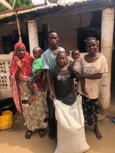 A family standing outside their home with a large sack, smiling and waving at the camera.