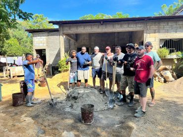Group of men posing with shovels at a construction site under clear blue sky.