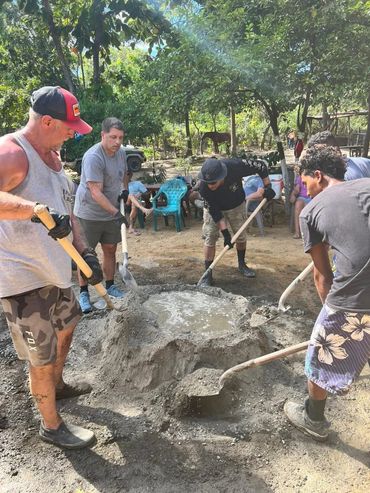 A group of men mixing cement outdoors under trees.