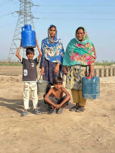 A family carrying water containers in a rural area under a clear sky.