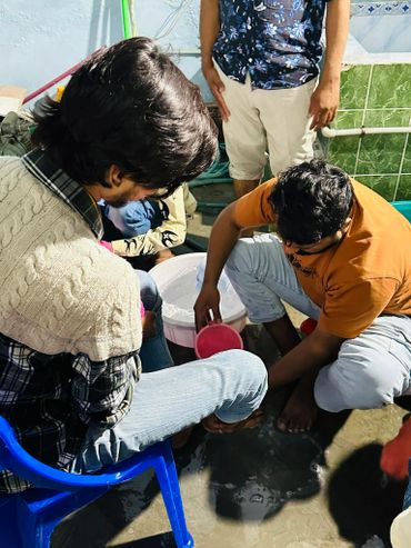 Group of young men washing feet in a bucket indoors.