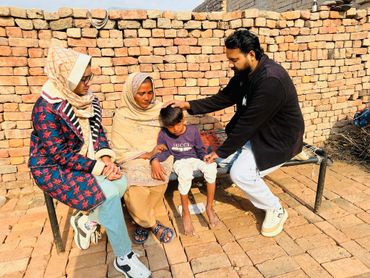 A man comforts a sad boy with two women sitting nearby against a brick wall.