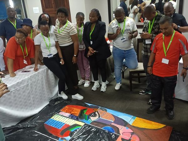Group of people observing a colorful abstract painting on the floor indoors.