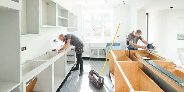 Two men installing kitchen cabinets in a bright room.