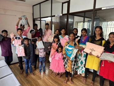 Group of children and adults holding clothes indoors.