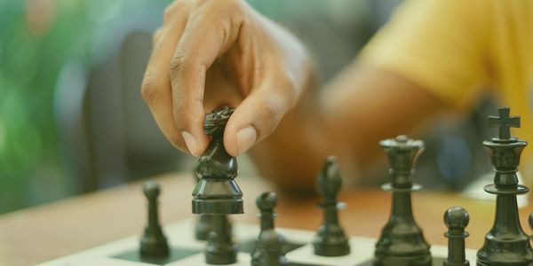 A hand lifting a chess piece off a chessboard.