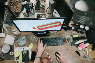 A picture of a computer on a desk with paper and pens also on the desk