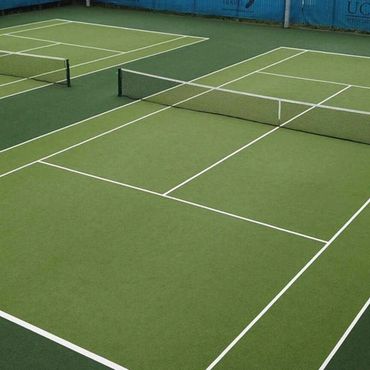 Two empty outdoor tennis courts with green surfaces and white lines.