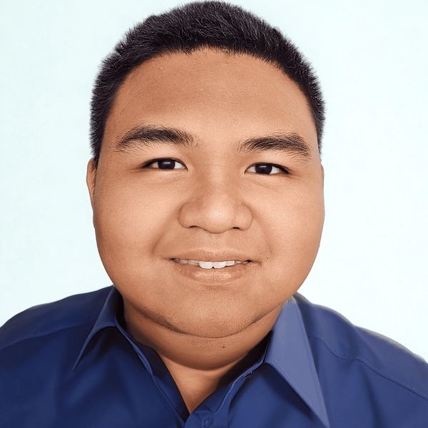 Smiling man in a blue collared shirt against a light background.