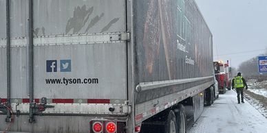 A Tyson semi-truck parked on a snowy roadside with a person walking nearby.