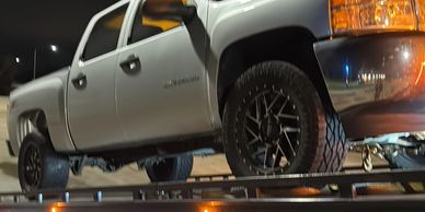 Silver pickup truck with custom black wheels parked at night.