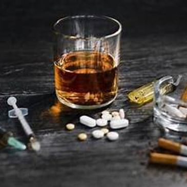 Glass of alcohol, pills, syringe, and cigarettes on table.
