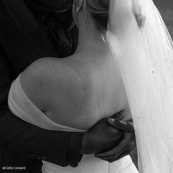 Photo d'un couple en noir et blanc et qui s'enlacent. Voile de mariée au vent avec perles.