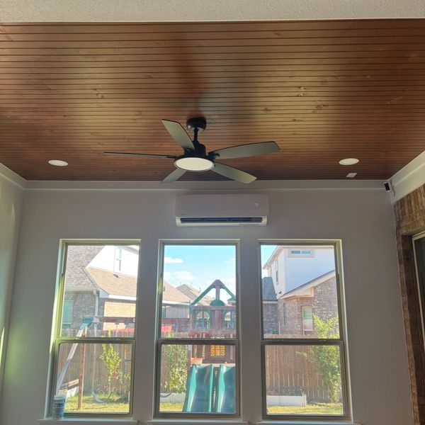 Ceiling fan in a room with three large windows showing a backyard.