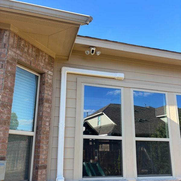 Exterior of house with security camera and windows reflecting sky.