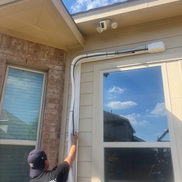 Person pointing to wiring on house exterior near security cameras.