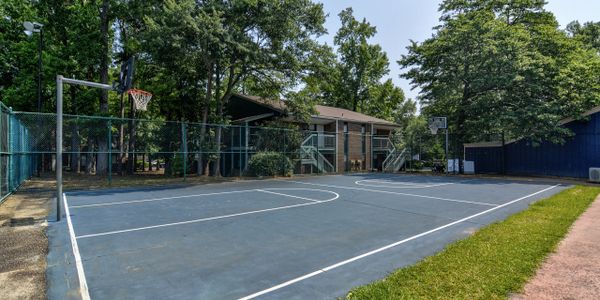 Empty outdoor basketball court surrounded by trees and buildings.