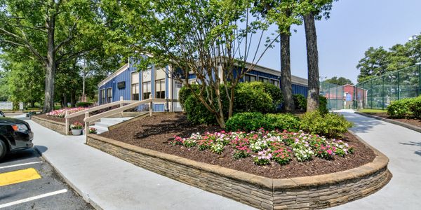 Well-maintained flower bed and pathway outside a blue building on a sunny day.