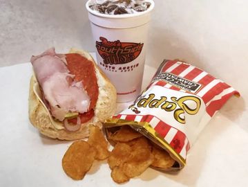 A sandwich, a bag of chips, and a cup of soda