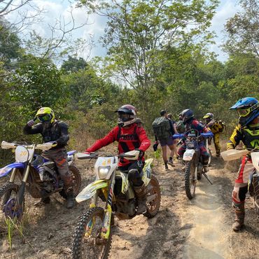 A group of motocross riders on dirt bikes taking a break in a forest trail.