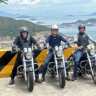 Four men on motorcycles posing by a scenic coastal view.