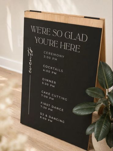 A black wedding schedule board with white text listing evening events.
