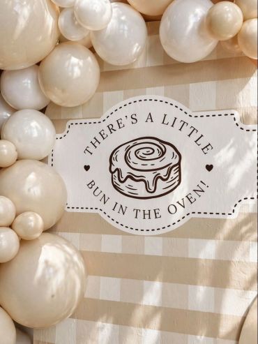 Cream-colored balloons surround a sign saying, 'There's a little bun in the oven!'