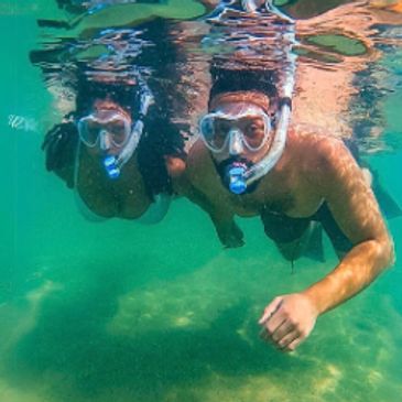 A couple snorkels without life vests side-by-side in tropical aquamarine water.
